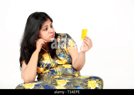 Frustriert schwangere Frau ist die Pille in der Hand mit dem Sitzen. Auf den weißen Hintergrund isoliert. Stockfoto