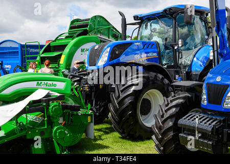 Anzeige von landwirtschaftlichen Maschinen (New Holland Traktoren, McHale Presse & Mäher) geparkten Seite an Seite auf den Handel stand-großen Yorkshire, England, UK. Stockfoto