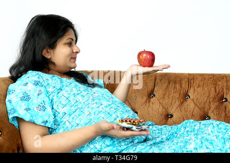 Schwangere Frau hält Medizin und Apfel in der Hand mit einem Lächeln begegnen. Auf den weißen Hintergrund isoliert. Stockfoto