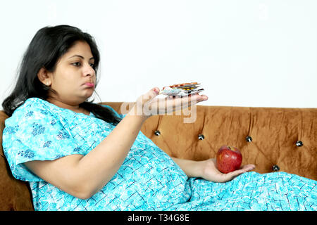 Schwangere Frau hält Medizin und Apfel in der Hand. Auf den weißen Hintergrund isoliert. Stockfoto