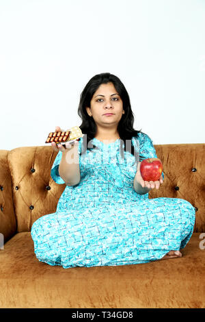 Bild der schwangeren Frau hält Medizin und Apfel in der Hand. Auf den weißen Hintergrund isoliert. Stockfoto