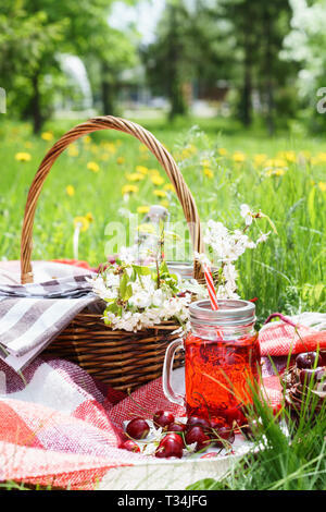 Kirschsaft in Mason jar und ein Picknick Korb mit Essen und Blumen im Hintergrund. Outdoor Picknick auf Gras. Stockfoto