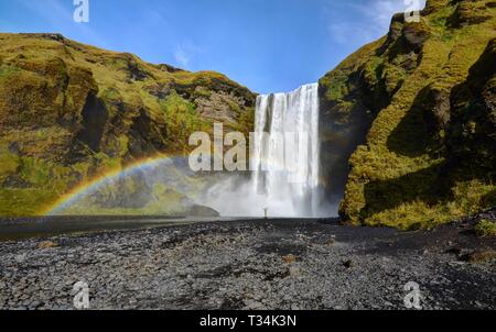 Mann stand unter einem Regenbogen am Wasserfall Skogafoss, Island Stockfoto