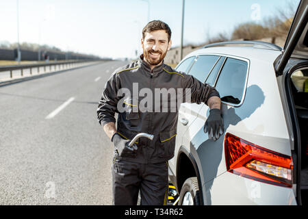 Porträt einer stattliche Straße Hilfe Arbeiter in Uniform in der Nähe von Den kaputten Auto auf der Autobahn Stockfoto