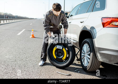 Pannenhilfe Arbeiter in Uniform ändern Auto Rad auf der Autobahn Stockfoto
