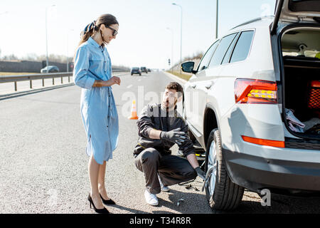 Pannenhilfe Arbeiter helfen jungen Frau ein Auto auf der Autobahn zu ändern. Stockfoto