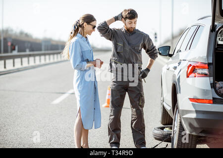Pannenhilfe Arbeiter in Uniform mit jungen Frau, die in der Nähe von Den kaputten Auto auf der Autobahn Stockfoto