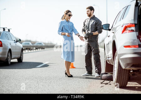 Pannenhilfe Arbeiter in Uniform mit jungen Frau, die in der Nähe von Den kaputten Auto auf der Autobahn Stockfoto
