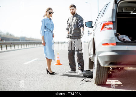 Pannenhilfe Arbeiter in Uniform mit jungen Frau, die in der Nähe von Den kaputten Auto auf der Autobahn Stockfoto