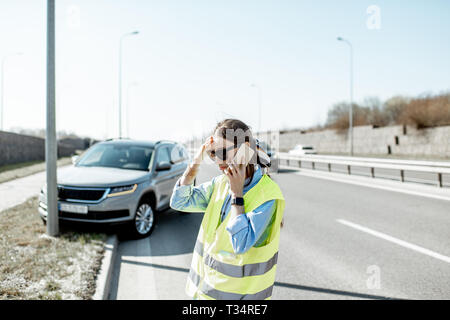 Peinlich, Frau Aufruf Pannenhilfe stehen in der Nähe des Autos während der Verkehrsunfall auf der Autobahn Stockfoto