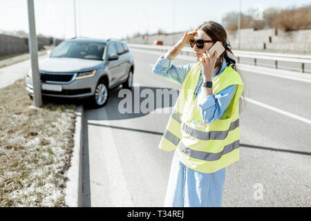 Peinlich, Frau Aufruf Pannenhilfe stehen in der Nähe des Autos während der Verkehrsunfall auf der Autobahn Stockfoto