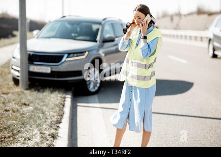 Peinlich, Frau Aufruf Pannenhilfe stehen in der Nähe des Autos während der Verkehrsunfall auf der Autobahn Stockfoto