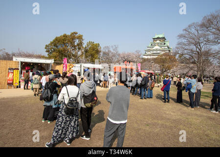 Die Menschen in der Warteschlange für Essen im Frühling hana-mi, Kirschblüte anzeigen, Festival am Nishinomaru Garten in der Burg von Osaka. Das Schloss im Hintergrund halten, mit blauem Himmel. Stockfoto