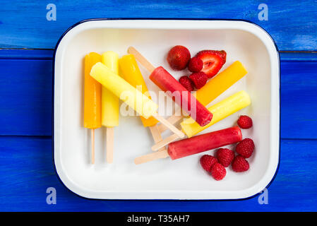 Eis, Orange, Erdbeer und Zitrone Eis am Stiel mit Beeren im Fach, auf blauem Hintergrund Stockfoto