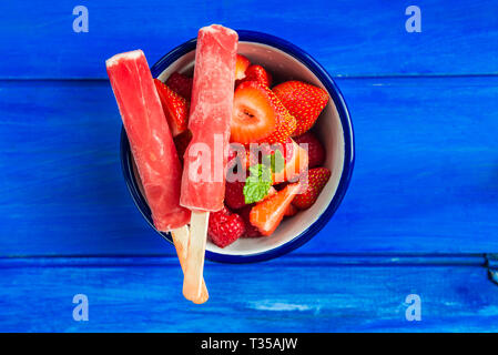 Helle Erdbeereis Eis am Stiel mit frischen Erdbeeren auf dem hölzernen Blauer Hintergrund Stockfoto