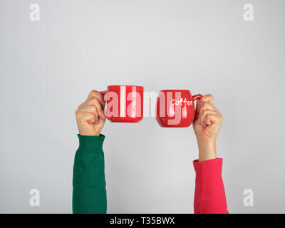 Zwei Hände in einem Pullover mit roten Keramik Becher auf weißem Hintergrund Stockfoto