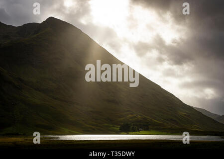 Sun Filterung durch Wolken, gezielt Teile des Tals in Glencoe, Schottland beleuchten. Stockfoto
