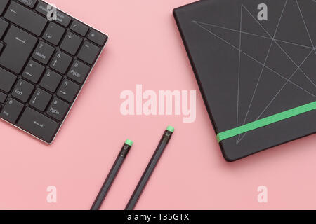 Ansicht von oben, Notizbuch und Bleistift mit Tastatur auf rosa Hintergrund. Close-up Stockfoto