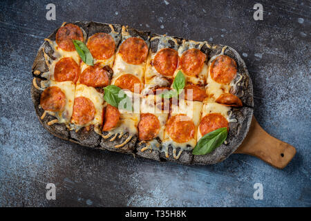 Pepperoni Pizza auf hölzernen Platte schwarz, Ansicht von oben Stockfoto