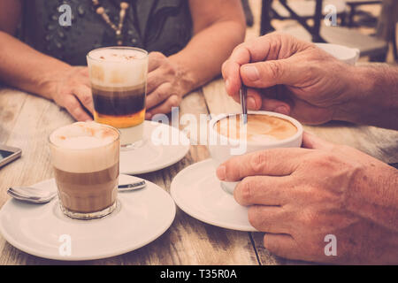 Nahaufnahmen der Hände mit Kaffeetassen in ein cafe bar mit Cappuccino für leckeres Frühstück am Morgen - gealterte Hände und reifes Paar haben eine Pause Stockfoto