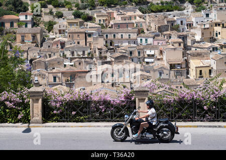 Mann reiten Motorrad in Hill City von Modica Alta in Richtung Modica Bassa, Sizilien, Italien suchen Stockfoto