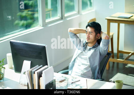 Junge asiatische Geschäftsmann Unternehmer betrachten im Amt, die Hände hinter dem Kopf runzelte die Stirn. Stockfoto