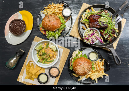 Burgersm Pommes frites, Ceviche, Rippen und Muffin auf einem Holztisch Stockfoto