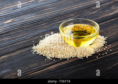 Sesamöl in Glasschale und Haufen Samen auf dunklen Holztisch Stockfoto