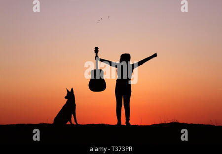 Silhouettegirls Gitarrist auf Sonnenuntergang Hintergrund, Silhouette einer Hunderasse Belgischer Schäferhund Malinois, glücklich, Freunde, outdoor Stockfoto