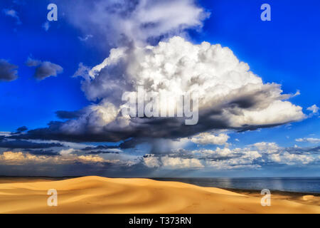 Turtle wie geformte stürmischen regen Cloud über Sanddünen an der Pazifikküste von Australien im blauen Himmel fällt Regen Stockton Strand menschenleer zu Dürren. Stockfoto