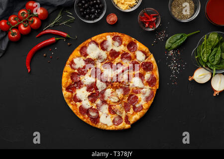 Hot Pepperoni Pizza und Zutaten zum Kochen auf schwarzem Hintergrund, Ansicht von oben Stockfoto