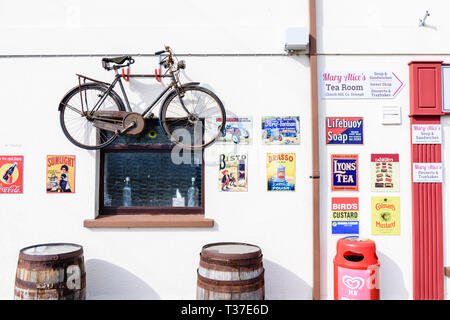 Ein Fahrrad- und ein altmodisches Metall werbeschilder an der Wand außerhalb eines Irish Shop. Stockfoto