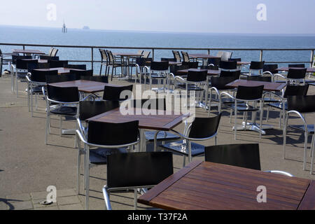 Tische und Stühle ohne Personen an der Seepromenade gegen Bodensee und Fähre und Rauszuschwimmen am Horizont, leeren Restaurant in frühen Autolöscher Stockfoto