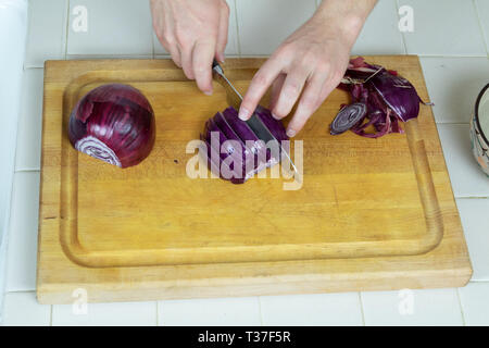 In der Nähe der Hände bei der Arbeit eine halbe rote Zwiebel schneiden auf einem Schneidebrett Schuß von oben. Stockfoto