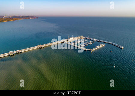 Polen, Sopot Resort. Hölzerne Seebrücke (Molo) mit Marina, Yachten, Segelboote und die Promenade. Far View von Gdynia in thw Hintergrund. Luftbild bei Sonnenaufgang Stockfoto