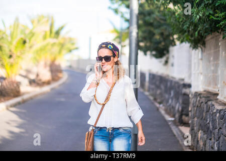 Hippy Menschen Porträt mit attraktiven Blondine mittleren Alters Frau wandern und am Telefon auf der Straße in Outdoor Freizeit - glückliche Mitarbeiter Stockfoto