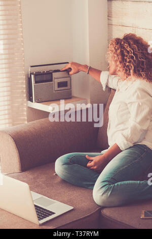 Mode cute Curly junge Frau zu Hause mit alten und neuen Technologien auf dem Sofa sitzen - vintage Konzept und Radio aus 80s-Leute im Hou Stockfoto