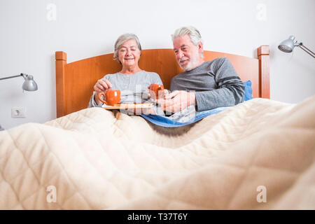 Alte senior Reife kaukasischen Paar genießen Frühstück am Morgen im Bett im Schlafzimmer zu Hause - Rentner zusammen leben und gesund zu essen Stockfoto