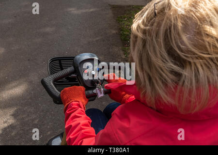 Ein über die Schulter geschossen von einer älteren Dame in einem roten Mantel, in der Freiheit eines elektrischen Mobilität scooter, drei Viertel der Kopf, Stockfoto