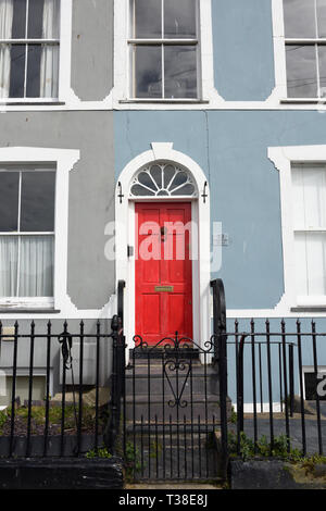 Pastellblau und grau Reihenhaus, weiße Steintür umgeben rote Holztür, Fanlight und verziertes schwarzes Eisenwerk in Caernarfon Nord wales uk Stockfoto