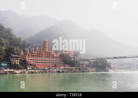 Rishikesh Indien. 10. Januar 2018. Nicht identifizierte Personen, Laxman Jhula Fußgängerbrücke auf dem Fluss Ganges durch die Tera Manzil Tempel bei Sonnenuntergang. Stockfoto