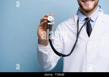 Hübscher junger Mediziner mit einem Stethoskop, über Hellblau isoliert. Stockfoto