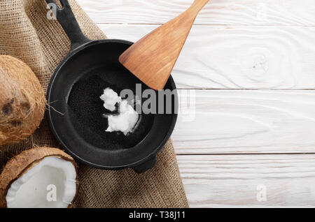 Kokosnuss, Shell mit Fleisch, Gusseisen Skillet und Spachtel auf Hanf Sack auf weißen Küche aus Holz Tisch Stockfoto