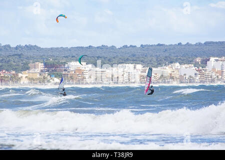 CAN PASTILLA, MALLORCA, SPANIEN - 6. APRIL 2019: Surfer in die grünen Wellen spielen an einem windigen, sonnigen Tag am 6. April 2019 in Can Pastilla, Mallorca, Sp Stockfoto