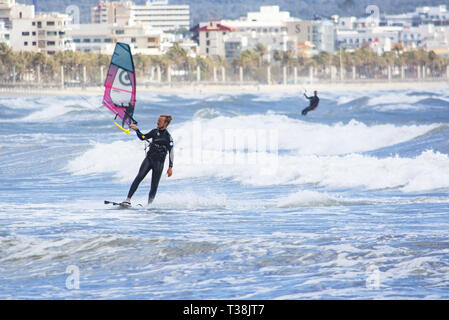 CAN PASTILLA, MALLORCA, SPANIEN - 6. APRIL 2019: Surfer in die grünen Wellen spielen an einem windigen, sonnigen Tag am 6. April 2019 in Can Pastilla, Mallorca, Sp Stockfoto