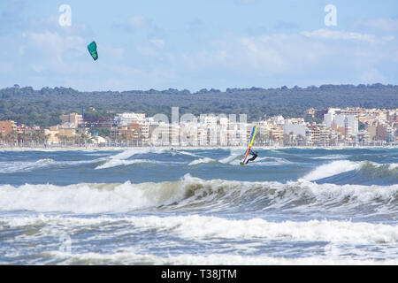 CAN PASTILLA, MALLORCA, SPANIEN - 6. APRIL 2019: Surfer in die grünen Wellen spielen an einem windigen, sonnigen Tag am 6. April 2019 in Can Pastilla, Mallorca, Sp Stockfoto