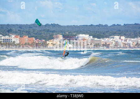 CAN PASTILLA, MALLORCA, SPANIEN - 6. APRIL 2019: Surfer in die grünen Wellen spielen an einem windigen, sonnigen Tag am 6. April 2019 in Can Pastilla, Mallorca, Sp Stockfoto