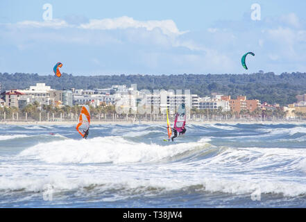 CAN PASTILLA, MALLORCA, SPANIEN - 6. APRIL 2019: Surfer in die grünen Wellen spielen an einem windigen, sonnigen Tag am 6. April 2019 in Can Pastilla, Mallorca, Sp Stockfoto