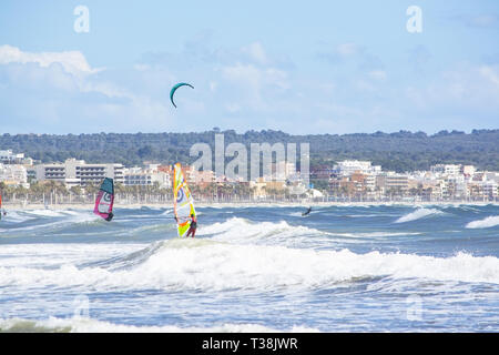 CAN PASTILLA, MALLORCA, SPANIEN - 6. APRIL 2019: Surfer in die grünen Wellen spielen an einem windigen, sonnigen Tag am 6. April 2019 in Can Pastilla, Mallorca, Sp Stockfoto