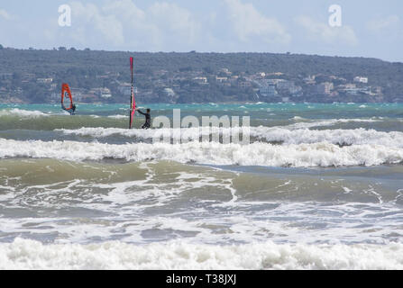 CAN PASTILLA, MALLORCA, SPANIEN - 6. APRIL 2019: Surfer in die grünen Wellen spielen an einem windigen, sonnigen Tag am 6. April 2019 in Can Pastilla, Mallorca, Sp Stockfoto